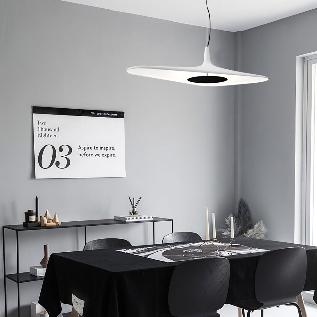 A white disc pendant with a dark centre hangs in a grey room above a black table and chairs, with a black console behind, from Clérachic.