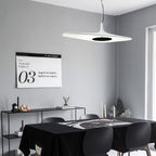 A white disc pendant with a dark centre hangs in a grey room above a black table and chairs, with a black console behind, from Clérachic.