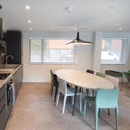 A black disc pendant hangs over an oval dining table with mint-green chairs in a bright kitchen and dining room, from Clérachic.