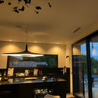 A black disc pendant glows over a dark kitchen island at dusk, with a large black-framed window behind, a Clérachic LED pendant.