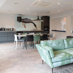 A black disc pendant hangs in a light open-plan kitchen and lounge with a mint-green sofa and a bird mural, from Clérachic.