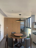 A black disc pendant hangs over a round dark dining table with a lazy Susan, against a pale oak wall, shown as this Clérachic pendant.