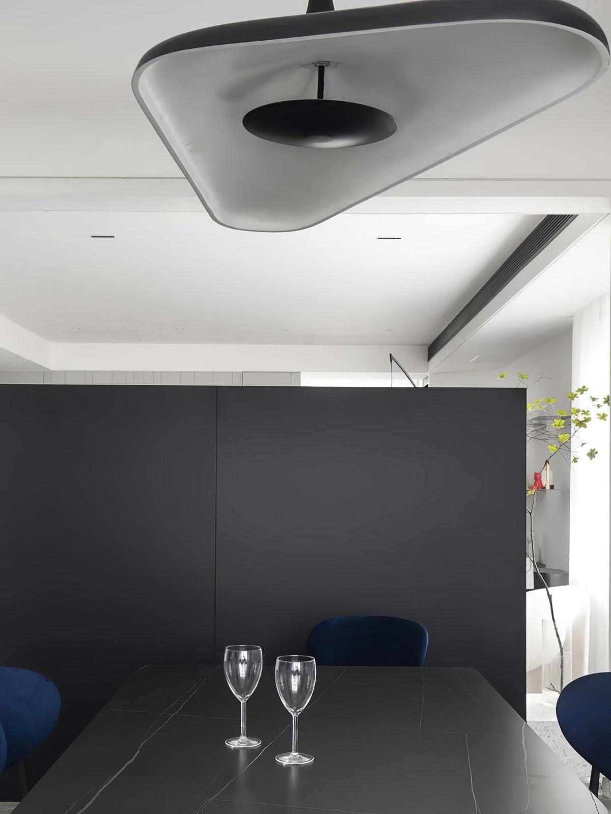 The underside of a grey disc pendant with a black centre hangs above a black table set with two wine glasses and navy chairs, from Clérachic.