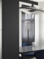 A white disc pendant fills the top of the frame above a black dining table with navy chairs and a wine glass, from Clérachic.