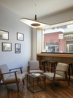 A white-lined disc pendant hangs beside a large window in a small seating nook with two armchairs and framed photographs, from Clérachic.