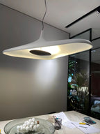 A white disc pendant with a glowing underside hangs low over a marble desk with papers and a bowl of white eggs, from Clérachic.