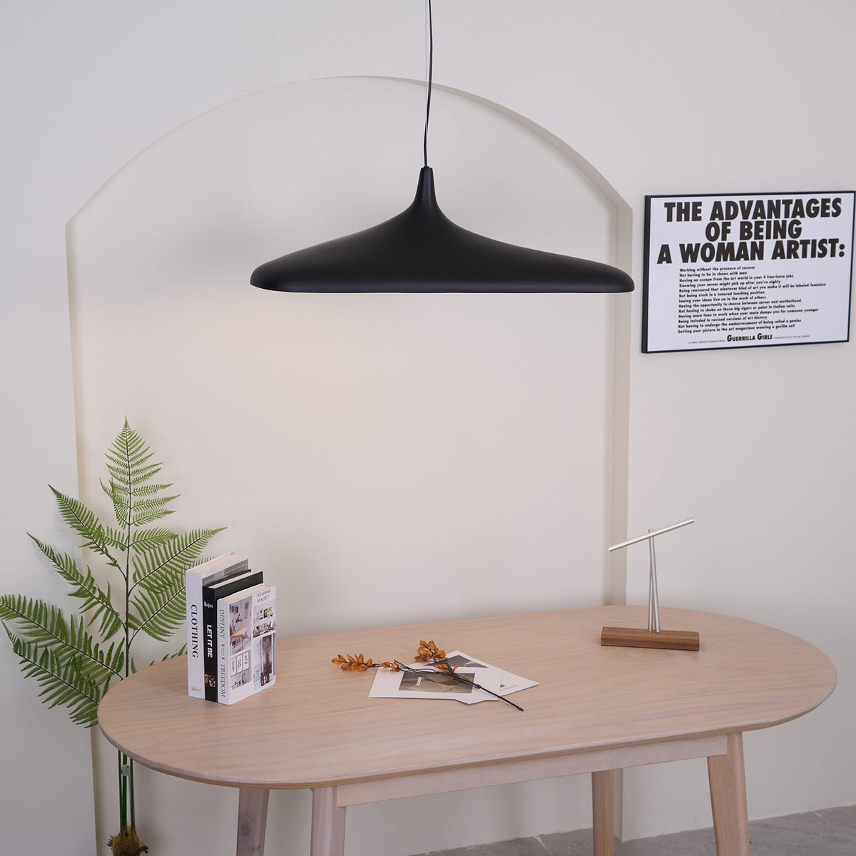 A black disc pendant hangs on a single cable above a pale oak table, in front of a white arch with a fern to one side, from Clérachic.