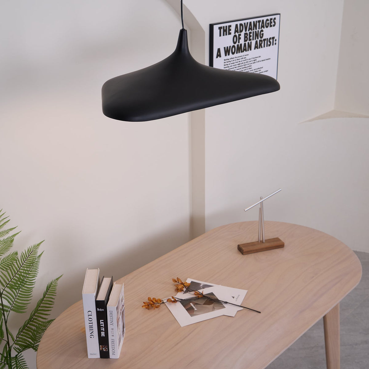 A black disc pendant seen from below left hangs above a pale oak table with books and dried flowers, a Clérachic LED pendant.