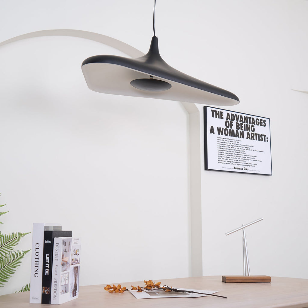 The underside of a black disc pendant with a pale inner surface is tilted toward the camera above a table with books, from Clérachic.