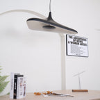 The underside of a black disc pendant with a pale inner surface is tilted toward the camera above a table with books, from Clérachic.