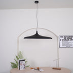 A black disc pendant with a round black ceiling canopy hangs straight on a long cable in front of a white arch, from Clérachic.