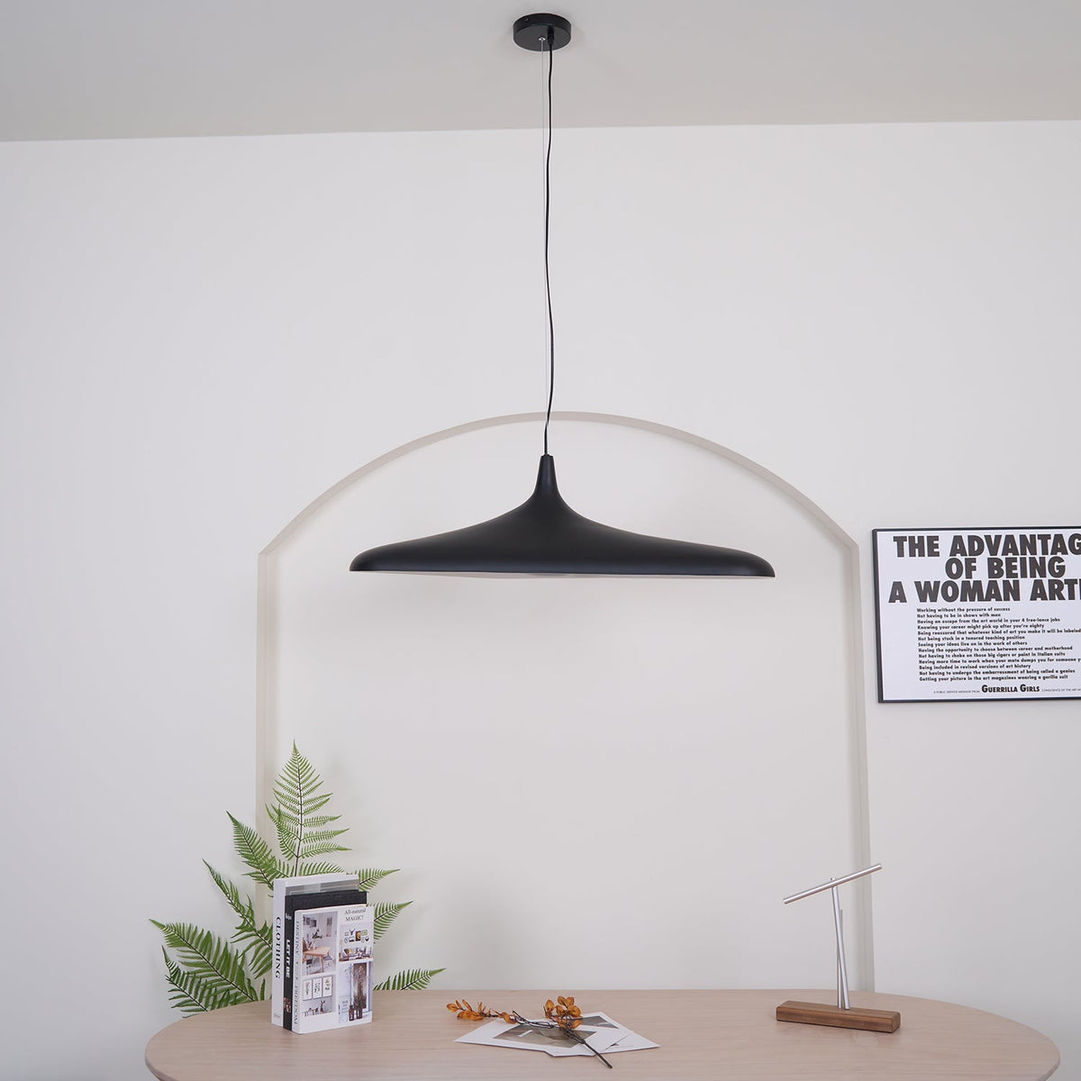 A black disc pendant with a round black ceiling canopy hangs straight on a long cable in front of a white arch, from Clérachic.