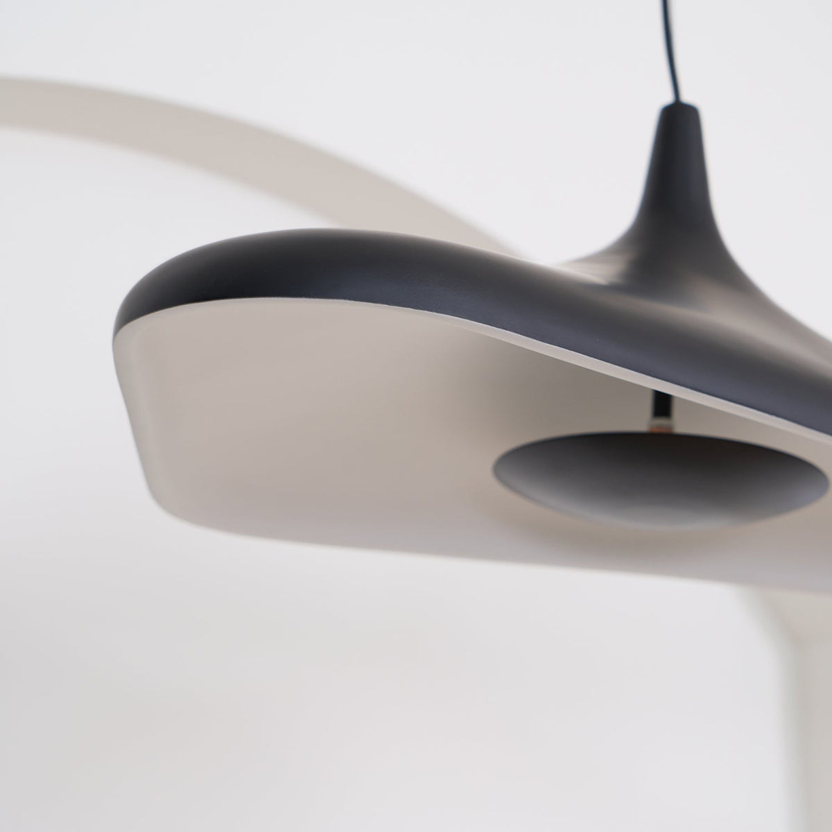 Close view of the black rim of this Clérachic disc pendant and its pale inner surface, with the dark centre plate in focus.