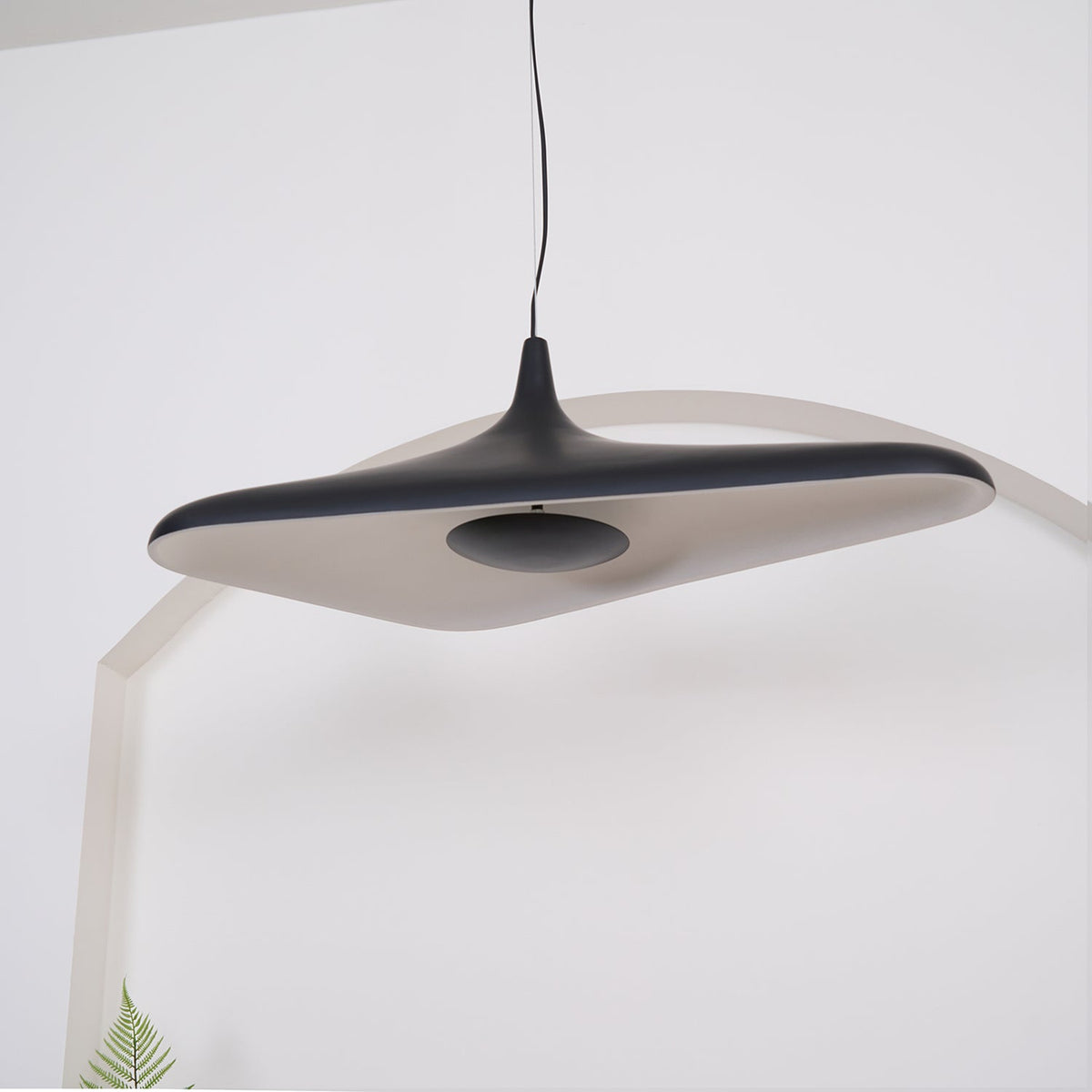 The underside of a black disc pendant shows a pale inner surface and a dark centre plate, hanging against a white arch, from Clérachic.