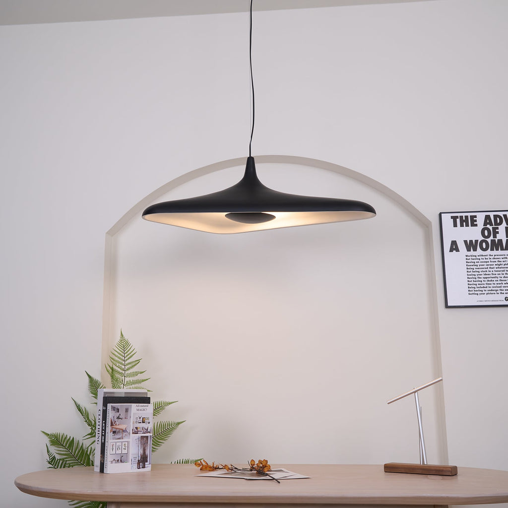 The same black disc pendant switched on, its pale inner surface glowing warm in front of a white arch, from Clérachic.