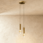 Clérachic two-head gold cylinder pendant with lit clear glass tips, hanging at staggered heights from a round gold plate.