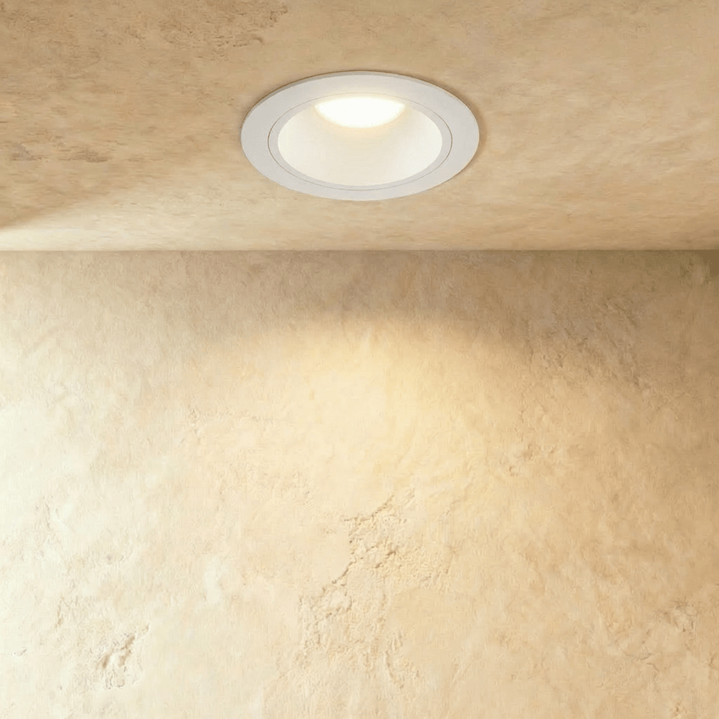 Clérachic round recessed downlight in a white trim and deep white cone, lit warm in a plaster ceiling above a textured wall.
