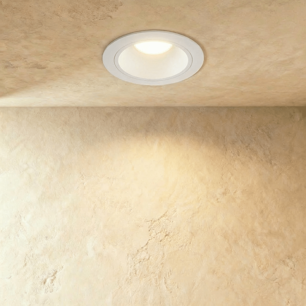 Clérachic round recessed downlight in a white trim and deep white cone, lit warm in a plaster ceiling above a textured wall.
