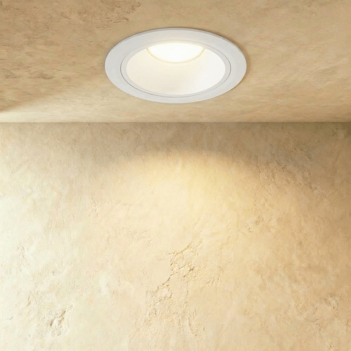 Clérachic white recessed downlight with a deep-set cone, glowing warm white and washing a limewash-textured wall below.