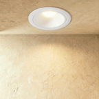 Clérachic larger white recessed downlight with a wide trim ring, casting a soft pool of warm light down a textured wall.