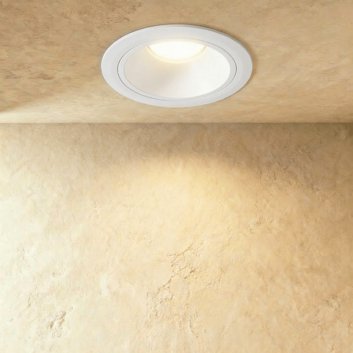 Clérachic larger white recessed downlight with a wide trim ring, casting a soft pool of warm light down a textured wall.