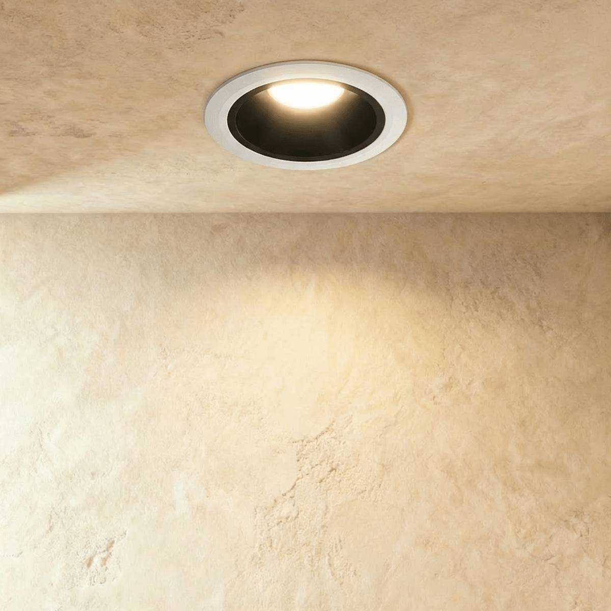 Clérachic recessed downlight with a white trim and black inner cone, lit warm white against a sand-coloured plaster wall.