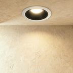 Clérachic medium recessed downlight with a white outer ring and black cone, glowing warm over a softly lit textured wall.