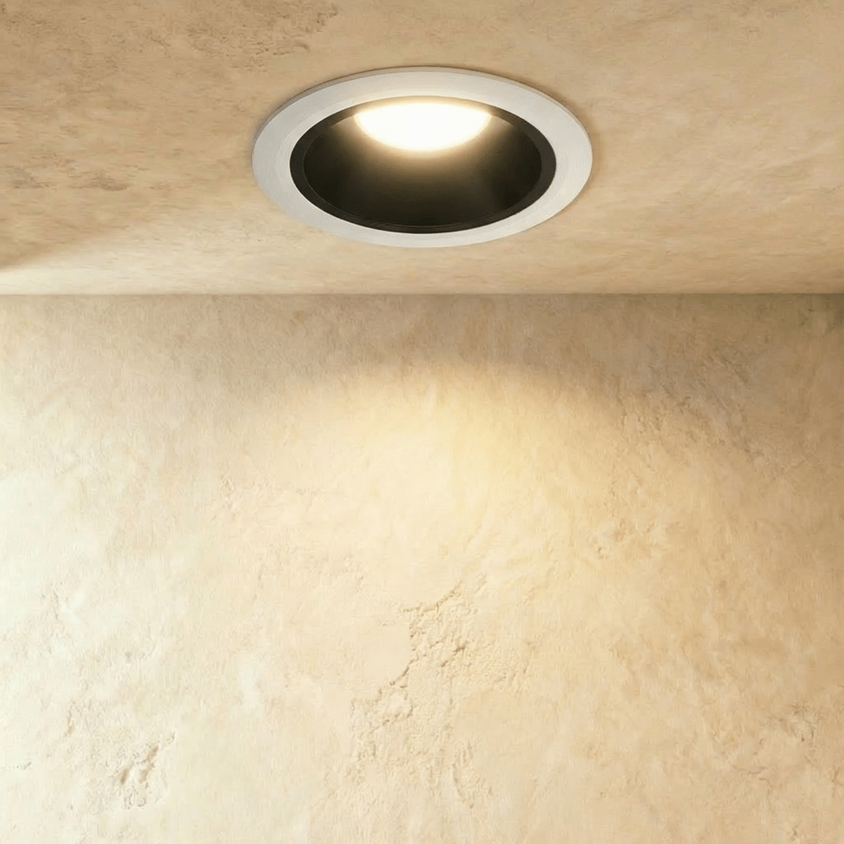 Clérachic medium recessed downlight with a white outer ring and black cone, glowing warm over a softly lit textured wall.