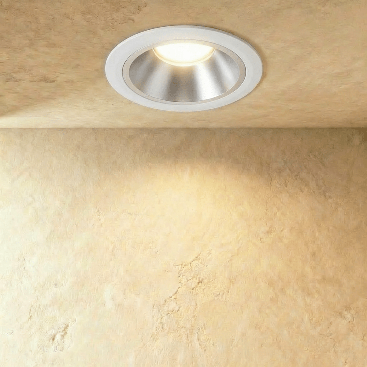 Clérachic large recessed downlight with a white trim and silver reflector, glowing warm above a textured sand-toned wall.