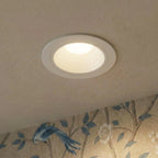 Clérachic white recessed downlight close up, its deep cone glowing warm on a ceiling edge beside a bird-print wallpaper.