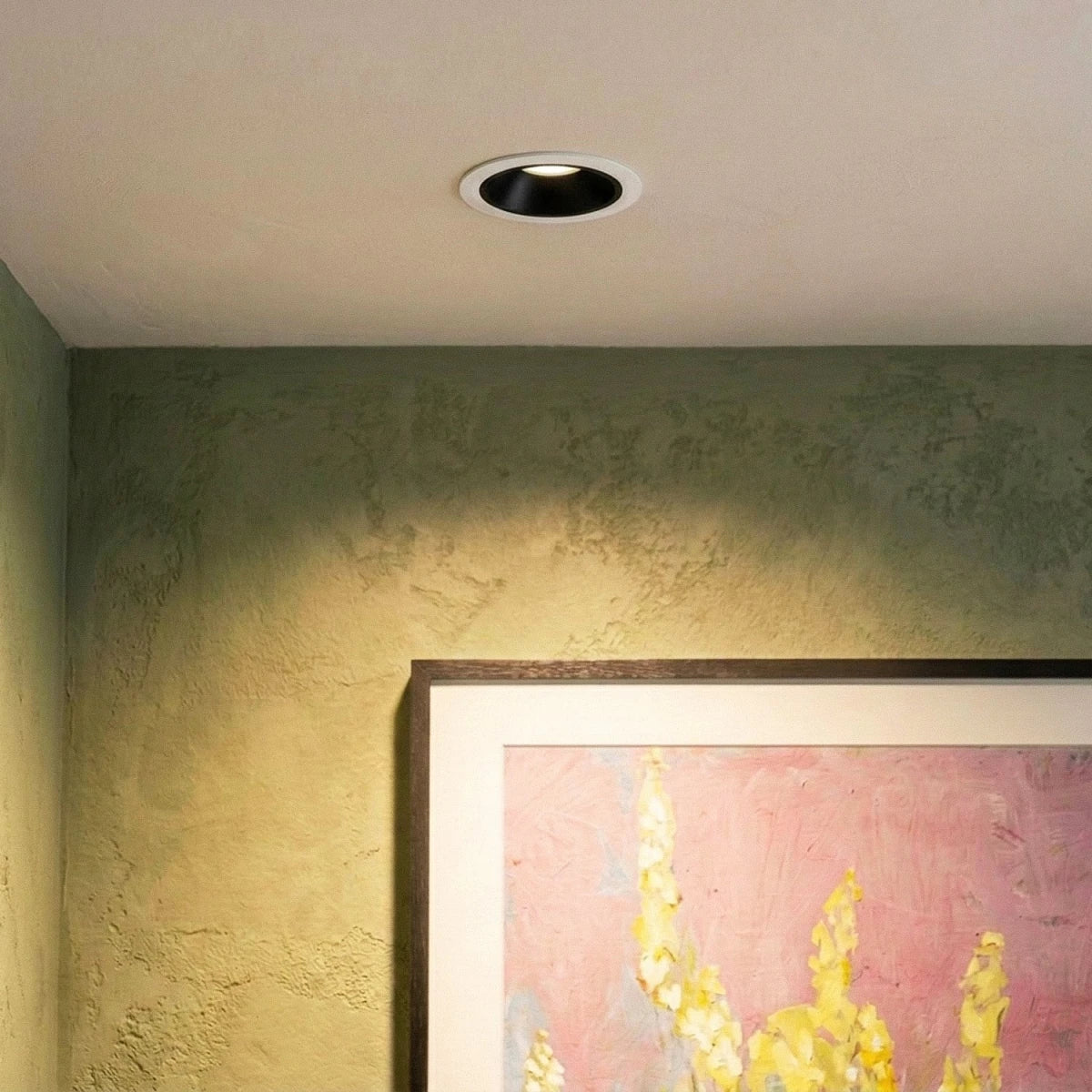 Clérachic recessed downlight with a white trim and black cone, washing a green plaster wall above a framed floral painting.