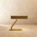 Clérachic Z-shaped brass table lamp with a flat slotted head, softly lit on a sand-toned limewash surface and wall.