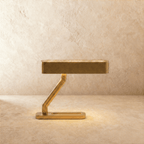 Clérachic Z-shaped brass table lamp with a flat slotted head, softly lit on a sand-toned limewash surface and wall.