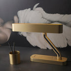 Clérachic satin brass table lamp with a Z-shaped arm and black inlay, on a dark desk beside a brass pen pot.