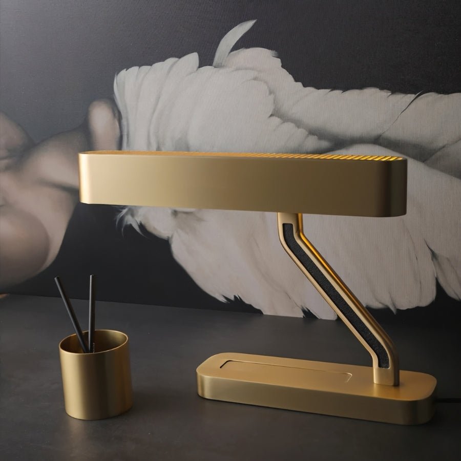 Clérachic satin brass table lamp with a Z-shaped arm and black inlay, on a dark desk beside a brass pen pot.