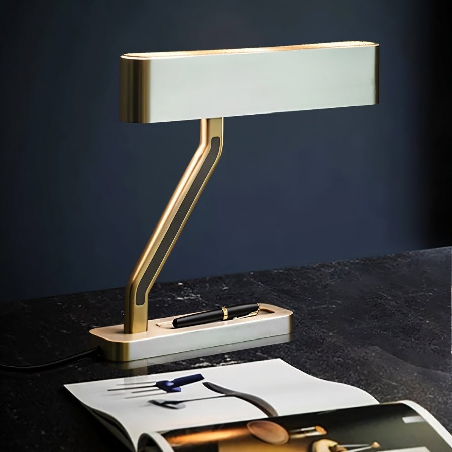 Clérachic table lamp with a pale head, brass edges and Z arm, on a black stone desk beside a fountain pen and open magazine.