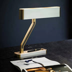 Clérachic table lamp with a pale head, brass edges and Z arm, on a black stone desk beside a fountain pen and open magazine.