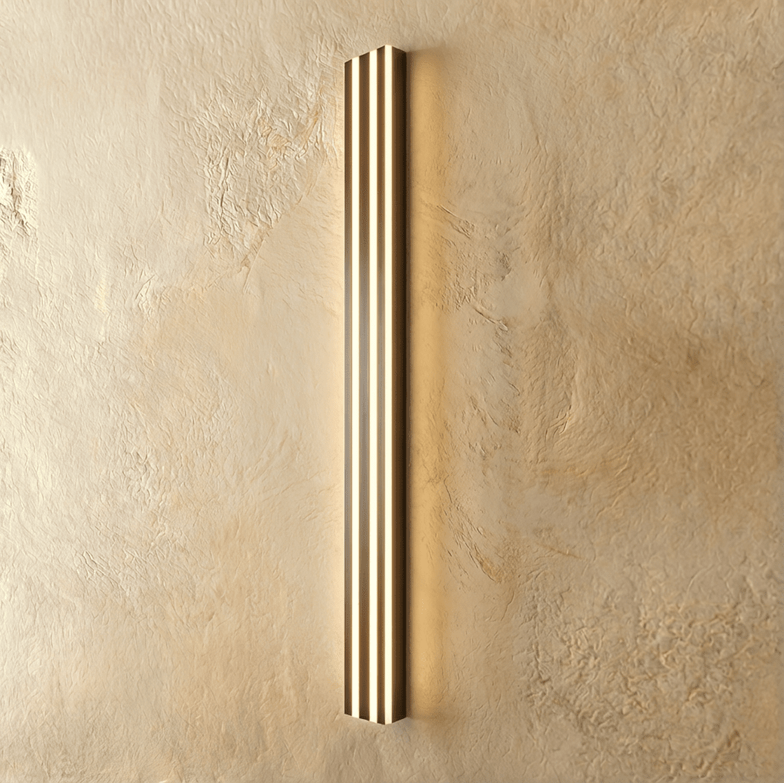 Clérachic slim black fluted LED bar wall light glowing warmly through three vertical light channels on limewash plaster.