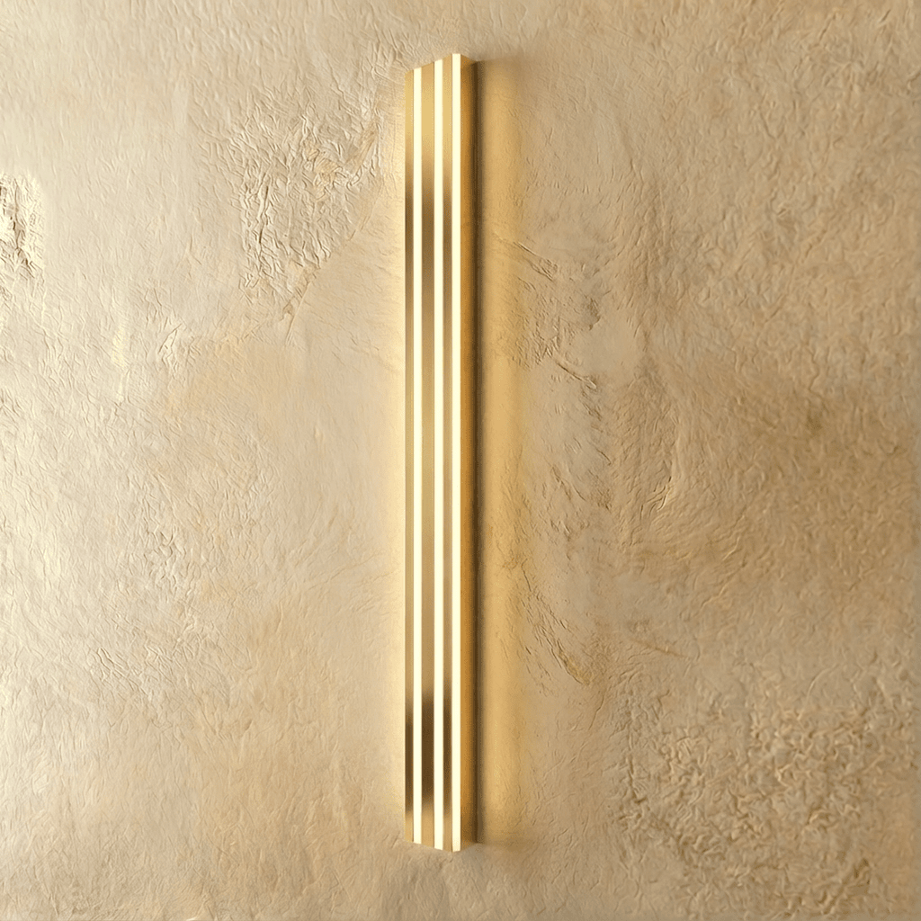 Clérachic slim gold fluted LED bar wall light lit, three bright vertical light channels on a warm plaster wall.