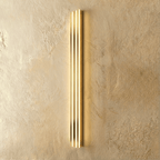 Clérachic slim gold fluted LED bar wall light lit, three bright vertical light channels on a warm plaster wall.