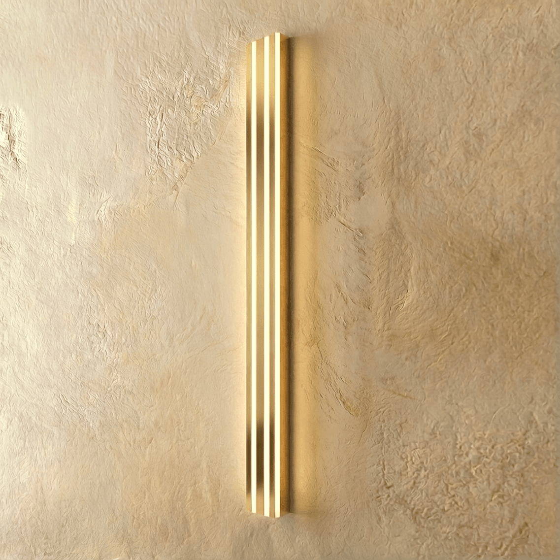 Clérachic slim gold fluted LED bar wall light lit, three bright vertical light channels on a warm plaster wall.
