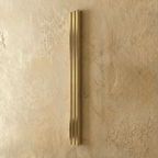 Clérachic slim gold fluted bar wall light switched off, brushed brass-tone ridges on a textured plaster wall.