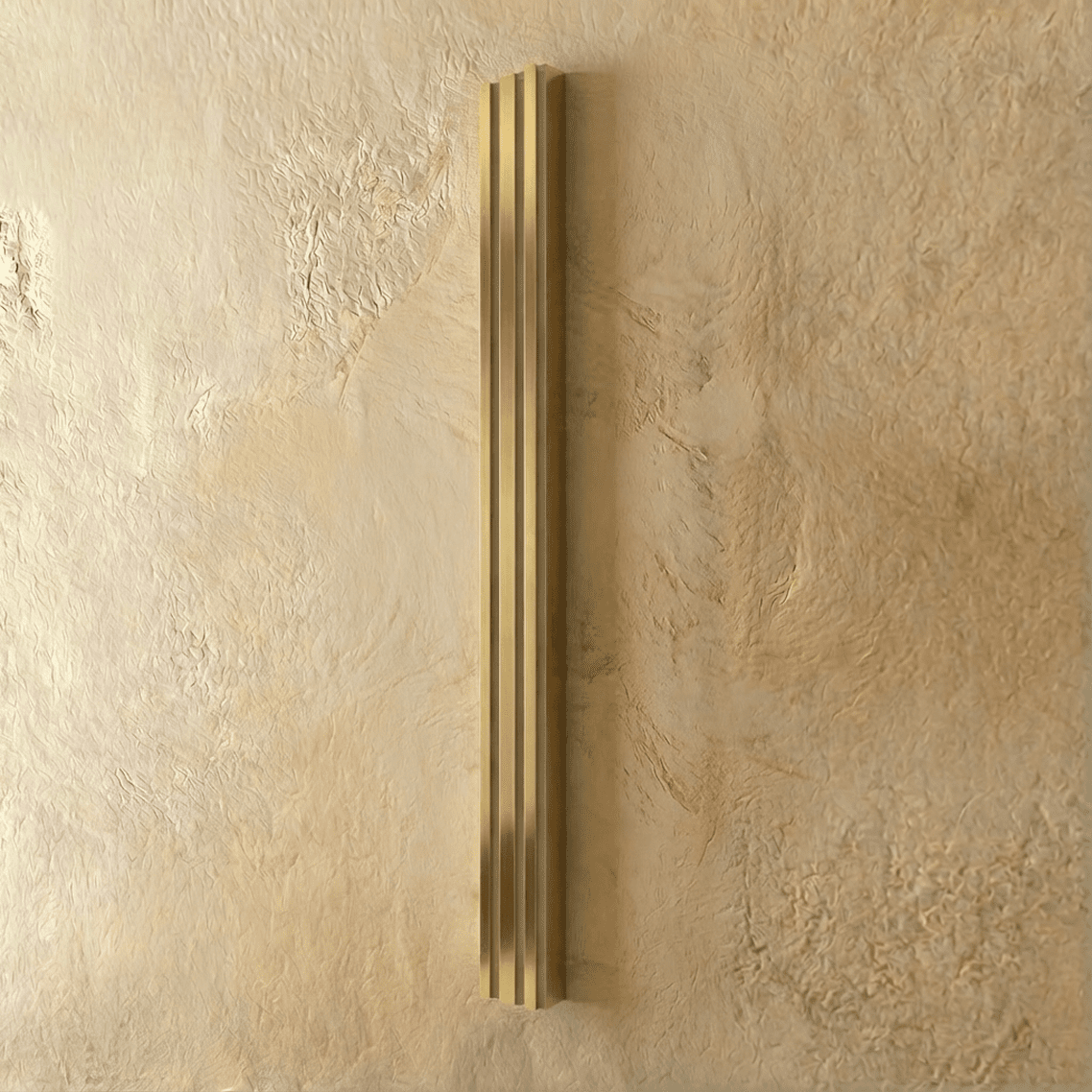 Clérachic slim gold fluted bar wall light switched off, brushed brass-tone ridges on a textured plaster wall.