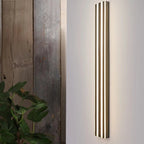 Clérachic tall dark fluted LED bar wall light lit on a pale wall beside weathered timber boards and a leafy plant.