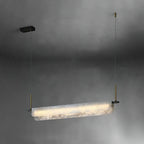 Three-quarter view of the Clérachic Linear Alabaster LED Pendant Light on a dark grey wall, showing the twin-lipped stone profile lit from within.