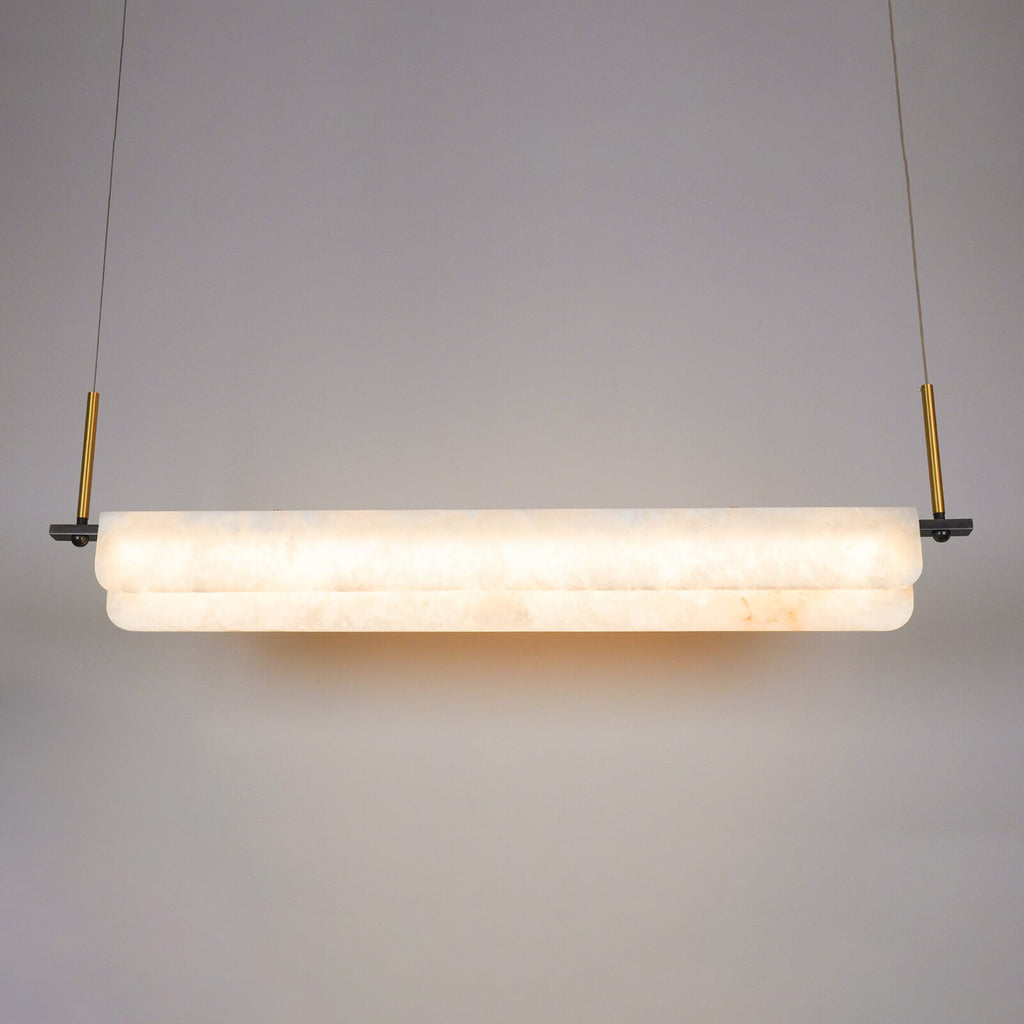 Clérachic Linear Alabaster LED Pendant Light lit head-on in the studio, warm light washing through the stone and pooling on the wall behind.