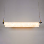 Clérachic Linear Alabaster LED Pendant Light lit head-on in the studio, warm light washing through the stone and pooling on the wall behind.