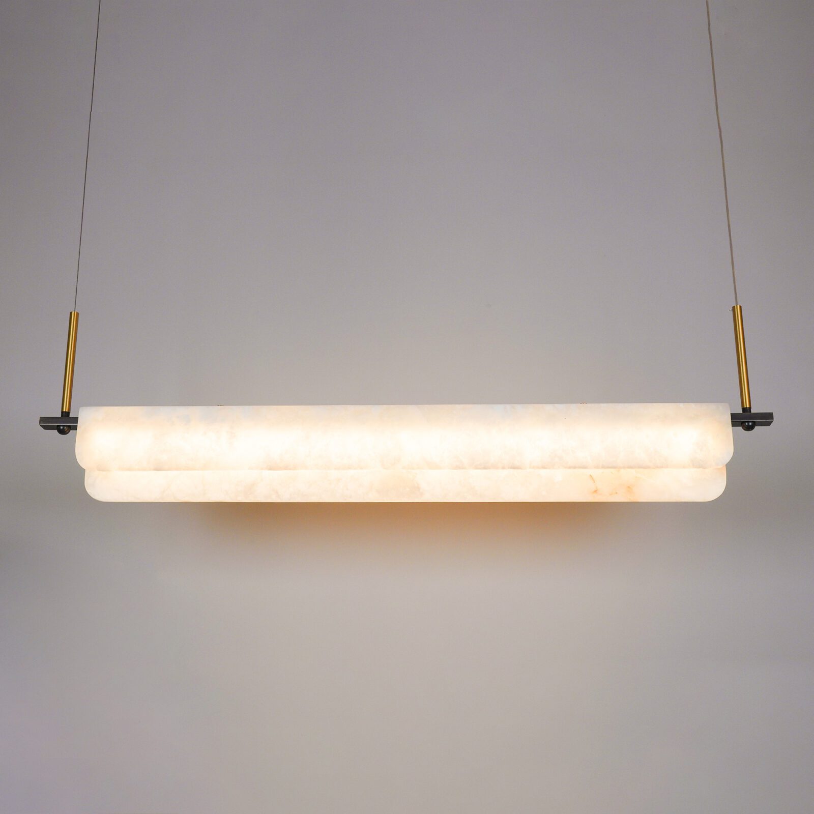 Clérachic Linear Alabaster LED Pendant Light lit head-on in the studio, warm light washing through the stone and pooling on the wall behind.