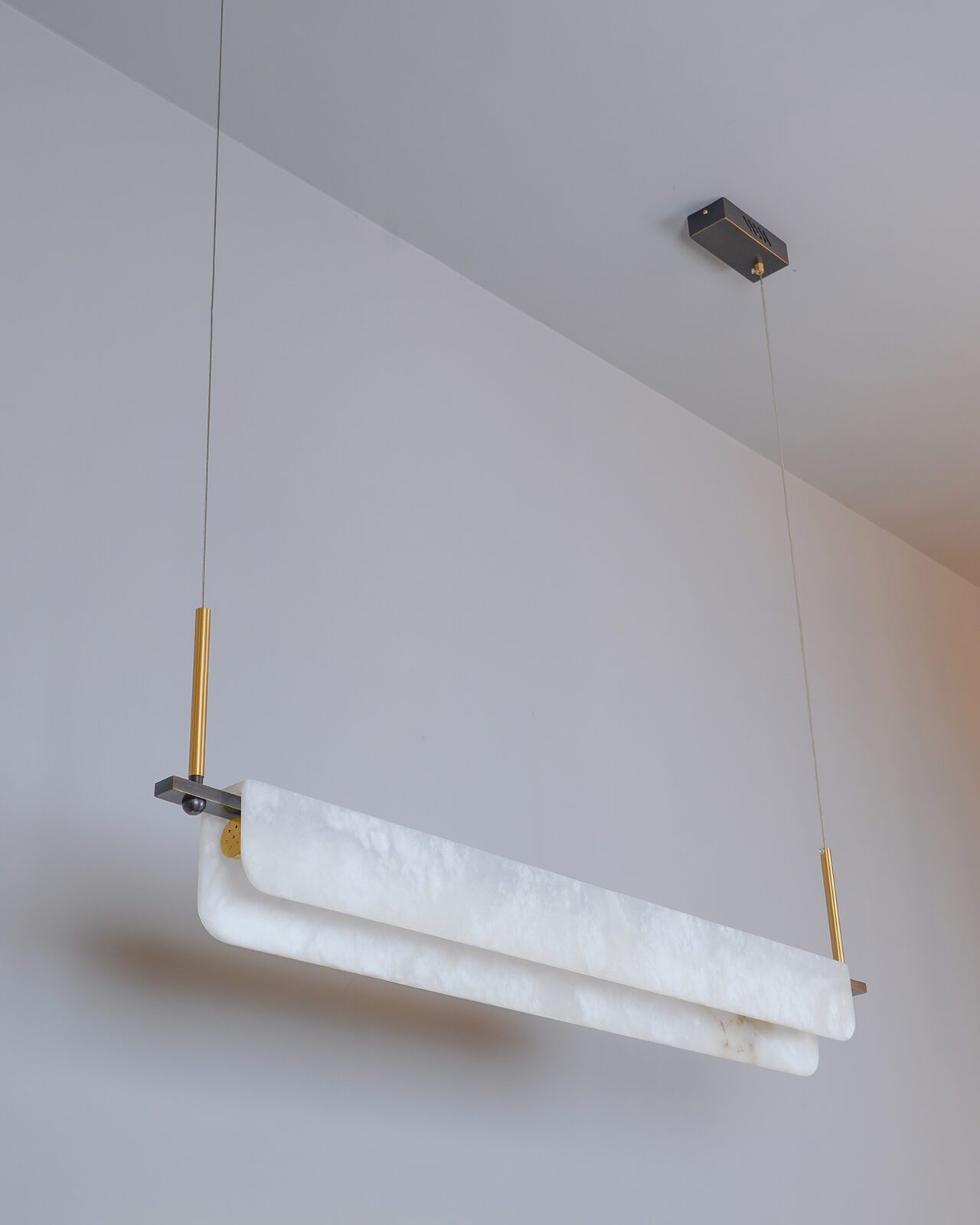 Underside view of the Clérachic Linear Alabaster LED Pendant Light on a white ceiling, brass droppers and blackened brackets holding the bar level.