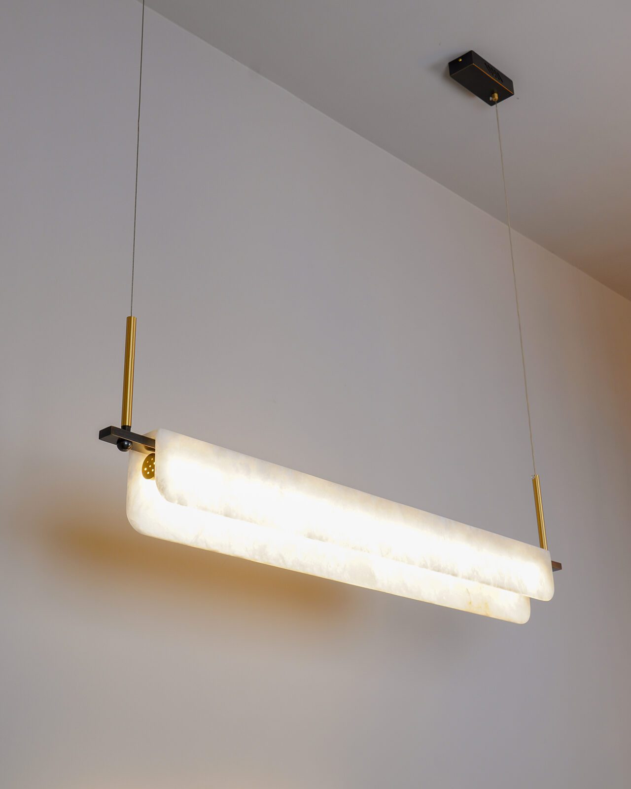 Clérachic Linear Alabaster LED Pendant Light in warm white, throwing a soft golden pool across the wall of a quiet dining corner.